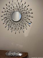 Photo of one large round silver starburst mirror mounted on wall with teardrop tips on metal spokes