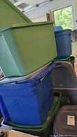 Stacked plastic storage bins in green, blue, teal, and gray, some with lids. Shown piled in garage setting.