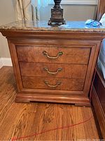 Front view of Thomasville side table showing three drawers with brass handles and marble top with wood grain body.