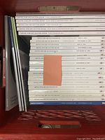 Photo showing a top view of a crate filled with Heffel Fine Art Auction House catalogs, mostly white spines showing titles and dates, reflecting various auction categories.