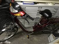 Side view of the vintage ECOLO electric bike showing red frame, front wire basket, black cushioned seat, and rear storage box.