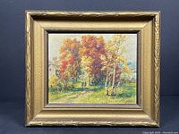 Framed fall landscape painting showing autumn trees with red, yellow, and green leaves, a pathway and two walking figures, signed bottom right.