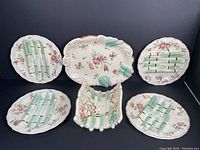 Full view of all six pieces in the set showing platter, asparagus stand, and four plates with floral and asparagus decoration on white ironstone.