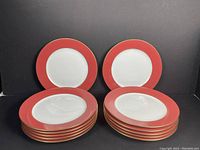 Front view of 12 Limoges porcelain plates stacked in two equal piles, showing poppy red rims and white centers.
