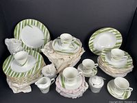 Full set layout in black background showing plates, cups, milk jug, and sugar bowl with green bamboo leaf pattern.
