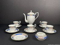Full display of all pieces in set: 5 cups, 6 saucers, sugar bowl, coffee pot