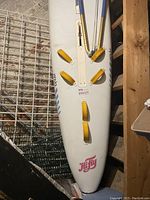 Top view of the white 12-foot Hifly windsurfing board with six yellow foot straps, pink Hifly logo, stored indoors.