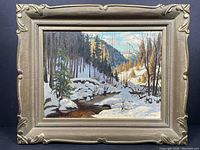 Full view of framed oil painting depicting a snowy stream, pine forest, and mountains, signed lower right.