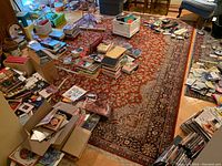 Full view of the rug laid on the floor surrounded by various books and household items, showing the overall design and condition.