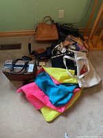 Photo showing assortment of bags piled against a wall, including colorful cloth bags, leather purses, and a white tote bag with Coca-Cola print.