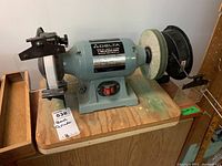 Full view of Delta bench grinder showing grinding wheel side with clear protective shield and mounted on wood surface.