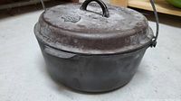 Side profile of cast iron Dutch oven with lid, showing weathered surface and bail handle
