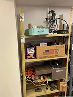 Shelf with multiple items including a cardboard box labeled 'ROUTER', extension cords, and small parts storage boxes