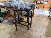 Side view of drop leaf table showing turned spindle legs and drop leaves extended with dishware on top.