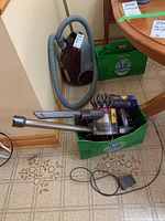 Main vacuum body and extension wand placed in box alongside burgundy canister vac (background)