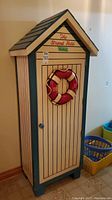 Front view of the nautical themed wooden cabinet with life preserver on door and 'The Strand Hotel' text.
