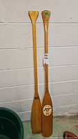 Two wooden canoe paddles leaning against a wall, showing length and overall condition.