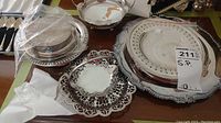 View of assorted silver-plated serving platters and plates stacked, showing decorative scalloped and pierced edge styles.