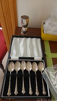 Six silver teaspoons in presentation box with shot glass behind