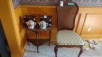 Wood demi-lune table with three turned legs next to Gibbard wood chair with cane back and upholstered floral seat. Small decorative boxes and ceramic house-shaped items on table are not included.