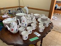 Full view of dinnerware set on table showing mugs, pots, sugar bowl, creamer and stacks of plates