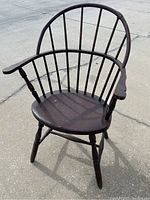 Full view of the dark brown antique Windsor chair showing curved back with spindles, armrests, and seated wooden base