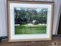 Framed color photograph of Augusta National Golf Course, showing lush golf course with bunker and azaleas in bloom, mounted in natural wood frame with white mat.
