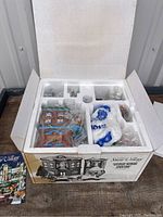 Open box showing contents inside original packaging with ceramic building, accessories and styrofoam inserts.
