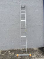 Straight position view of Krause 12 foot adjustable aluminum stick ladder with orange feet resting against wall.