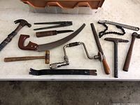 Various miscellaneous hand tools including claw hammers, hand saw, mallet, hand drill, rasp, and chain pipe wrench.