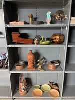 Photo showing shelves with various home decor items including wood boat, ceramic vases, brass figurines, plates.