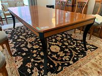 Angled view of full dining table showing wood veneer top and curved black legs