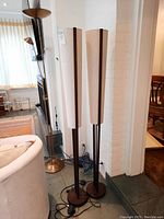 Two dark brown metal floor lamps with off-white fabric shades positioned side by side near a white brick wall.