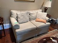 Front angle view of beige Ethan Allen loveseat with 3 throw pillows placed on seat cushions