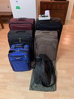 View of all six bags arranged in two rows on wood floor: five rolling luggage bags and one duffel bag in front