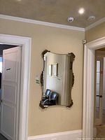 Front view of large, ornate framed wall mirror mounted on a beige wall, showing full mirror and its decorative frame.