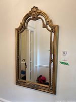 Front view of the ornate framed wall mirror hung against a light-colored wall, showing the overall shape and design.