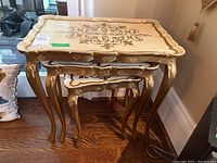 Set of three nesting tables stacked, showcasing the carved legs and ornate painted tops