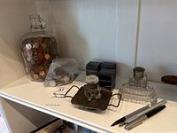 Shelf showing large glass jar filled with pennies, zip-lock bag of assorted coins, glass inkwells including one on a metal stand, three Yard-O-Led ink boxes, and three pens