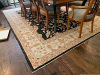 View of rug under dining table showing cream border with red and green floral motifs and black central field