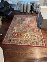 Full view of the rug placed on a wooden floor with office furniture nearby. Shows overall pattern, colors, and condition.
