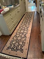 Full view of fringed Persian-style runner laid in hallway showing black field with beige floral border and fringe ends
