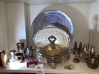 Wide angle photo showing the entire shelf of various silver plated items including trays, lidded dish, assorted cups, and small boxes.