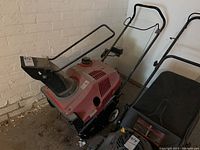Front and left side view of red Honda HS520 snow blower next to brick wall