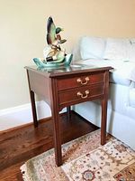 Front and side view of Stickley wooden end table with two drawers and brass hardware, placed on a patterned rug next to a blue couch.