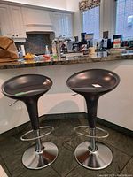 Two black swivel stools side-by-side under a kitchen counter with chrome bases and footrests.