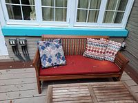 Front view of teak outdoor couch on deck with red seat cushion and four decorative pillows