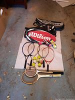Photo of all tennis rackets, tennis balls, and two racket covers laid flat on the floor
