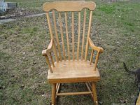 Front view of the wooden baby rocking chair outdoors on grass, showing vertical slats and armrests.