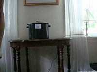 Full view of the large black enamel canning kettle on wooden table beside window with narrow curtains.